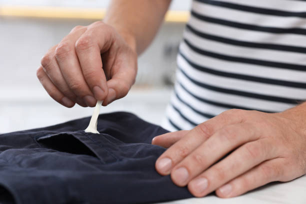 istock Man removing chewing gum from black jeans at white table indoors, closeup 1806452366
