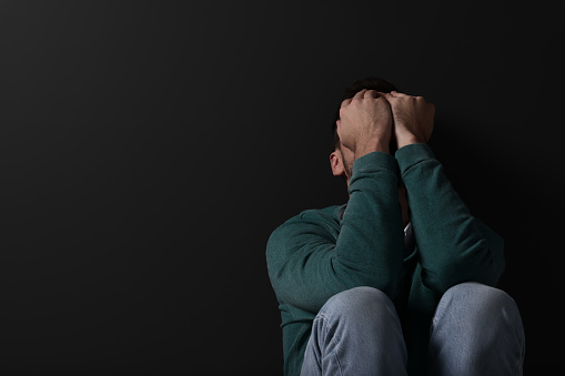 Upset man sitting on black background. Space for text