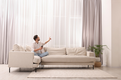 Man using smartphone on sofa near window with beautiful curtains in living room