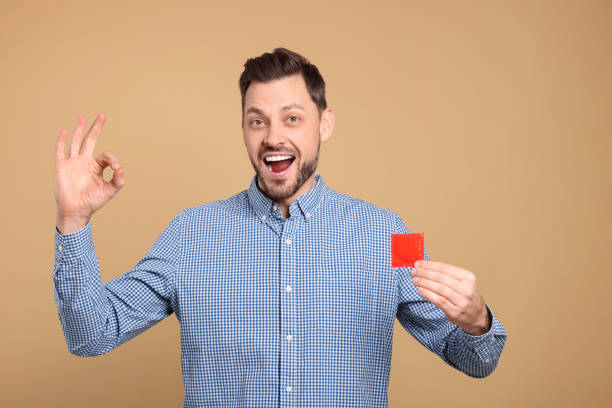 istock Excited man with condom showing ok gesture on beige background 1806471949