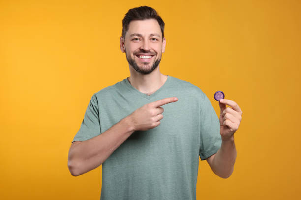istock Happy man holding condom on orange background 1806472581