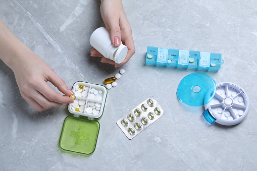 Woman putting pill into plastic box at grey marble table, top view