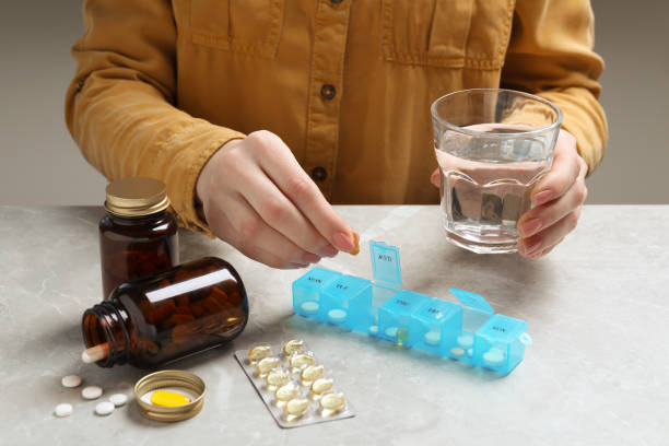 istock Woman putting pill into weekly organizer at grey marble table, closeup 1806481737