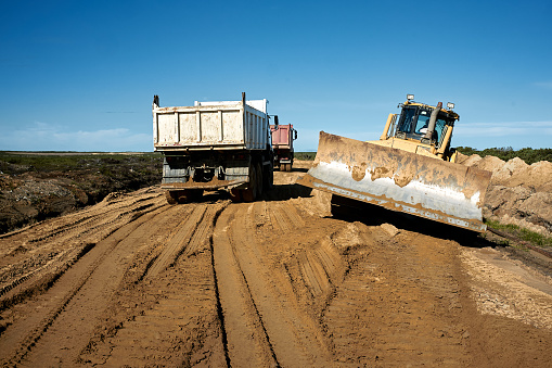 The bulldozer and dumper levels and compacts the clay soil for the base of the highway