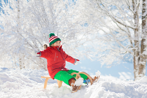 Little boy enjoying a sleigh ride. Child sledding. Toddler kid riding a sledge. Children play outdoors in snow. Kids sled in the Alps mountains in winter. Outdoor fun for family Christmas vacation.