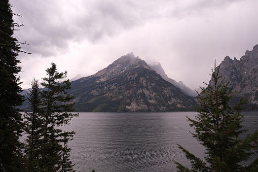 Jenny Lake located inside Grand Teton National Park.  Landscape photos of alpine lake surrounded by Teton mountains and evergreen trees.  Misty morning of cloud skies and clean clear water of the lake.  Bluish green color when the sun is shining.