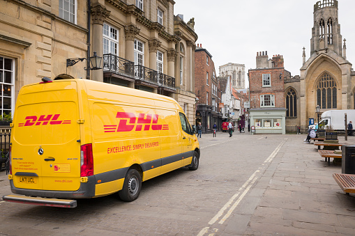 YORK, UK - April 19, 2023. Yellow DHL delivery van, courier driving through city centre.