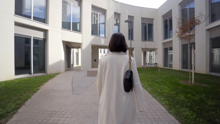 Camera follows business woman in formal suit going to work through a path of modern buildings