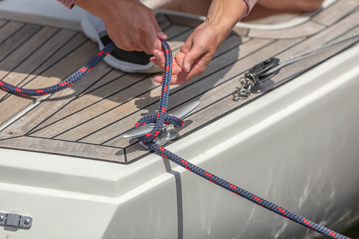 Hands tying a cleat hitch on a white sailing boat