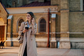Stylish female walking in the city and holding a mobile phone in her hands