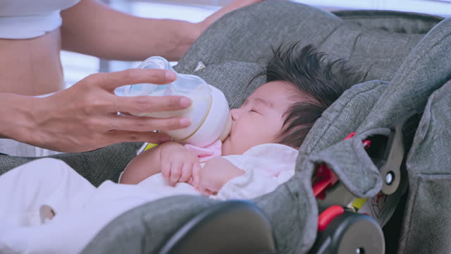 Little child drinks large bottle of milk in gray child seat.