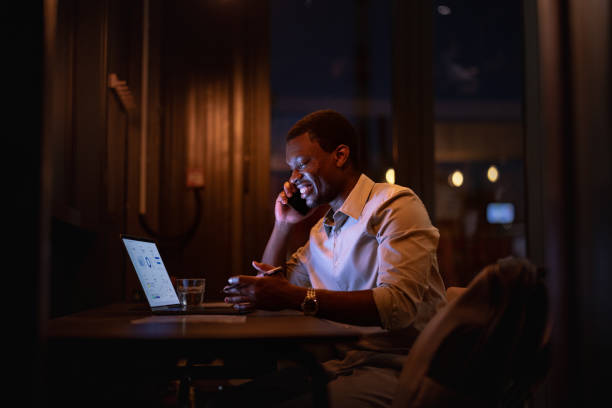 istock Happy Businessman Talking On A Mobile Phone And Using A Laptop At Night 1806693640