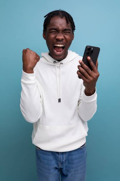 istock happy young african guy in white sweatshirt won online contest using smart phone 1806710775