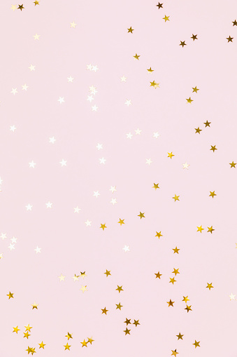 Gold sparkle confetti stars on a pink pastel background. Glitter, shine, bright. Christmas festive flat lay, winter holiday, new year, happy birthday concept. Flat lay, top view, copy space