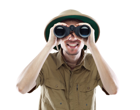 Young smiling man wearing pith helmet looking through binoculars, isolated on white