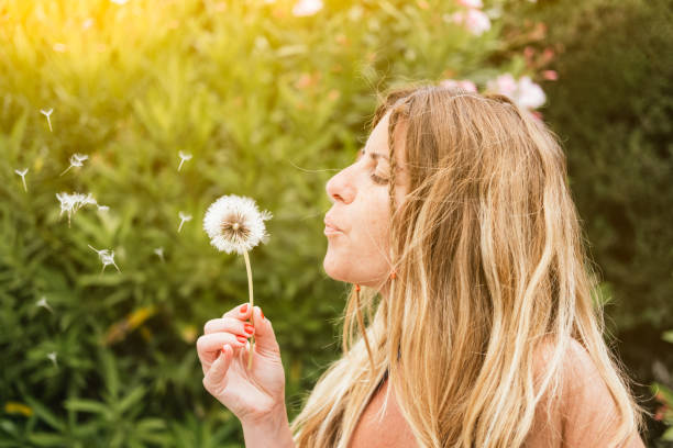 istock woman blowing a dandelion flower making a wish at sunset 1806739502
