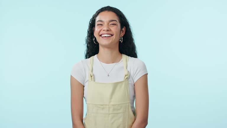 Happy, woman and laughing face with gen z, style and modern fashion in a studio. Funny joke, portrait and female person from Brazil with smile and blue background with confidence and trendy clothes