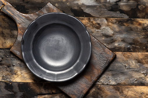 Empty black plate on wooden cutting board and old wooden background. With copy space, top view