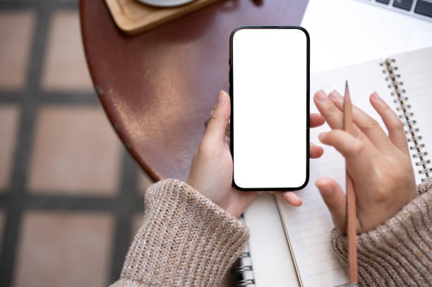 istock A woman is taking notes in her notebook and using her smartphone while sitting at a table outdoors. 1806885761