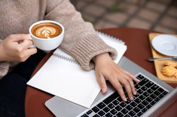 A woman is working remotely at a cafe, sipping hot coffee while working on her laptop.