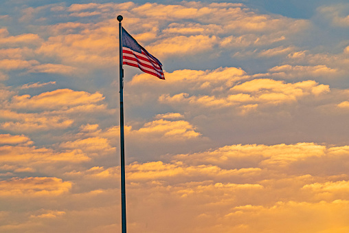 Litchfield, IL, USA – 01/21/2022: An American flag at dawn with the rising sun creating orange clouds over Litchfield's Lou Yaeger Lake.