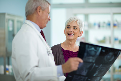 Male doctor showing x-ray image to cheerful mature woman at clinic. Horizontal shot.