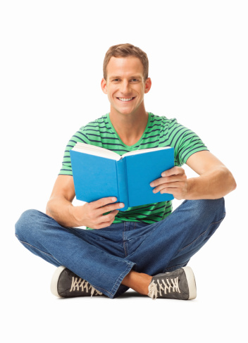 Portrait of a young man in casual wear sitting cross-legged with book on floor. Vertical shot. Isolated on white.