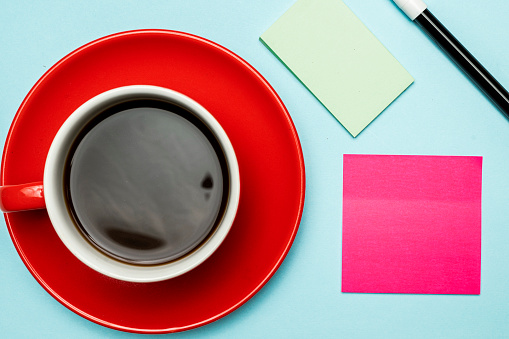 A cup of coffee and notepaper with marker on a colored background