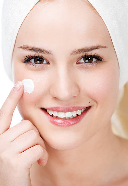 istock Beautiful young woman applying cream on her face 180696750