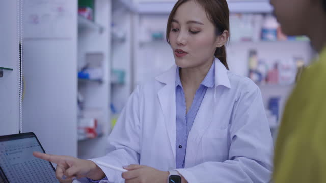 Young professional pharmacist showing tablet while helping beautiful female customer for recommendation and advice about medicine at pharmacy drugstore.