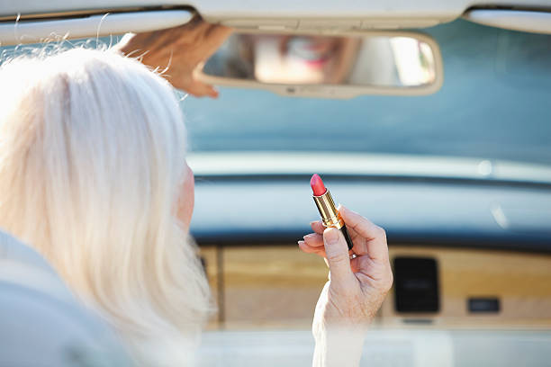 senior frau anwenden lippenstift im cabrio - outdoors car convertible wealth stock-fotos und bilder