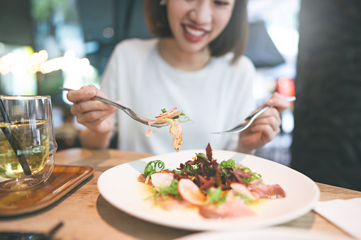 Japanese food Sashimi tuna vegetable salad. Asian woman background at indoor restaurant on day. City people foodie lifestyle on weekend concept.