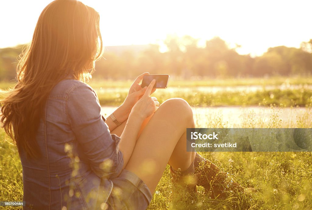 Woman enjoying the sun. Woman enjoying the sun outdoors in sunset, using her smartphone.. 30-39 Years Stock Photo