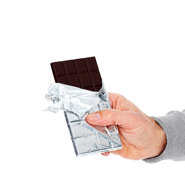 Man's hand holding a chocolate bar against white Closeup image of man's hand holding a chocolate bar against white background man hand holding candy bar stock pictures, royalty-free photos & images