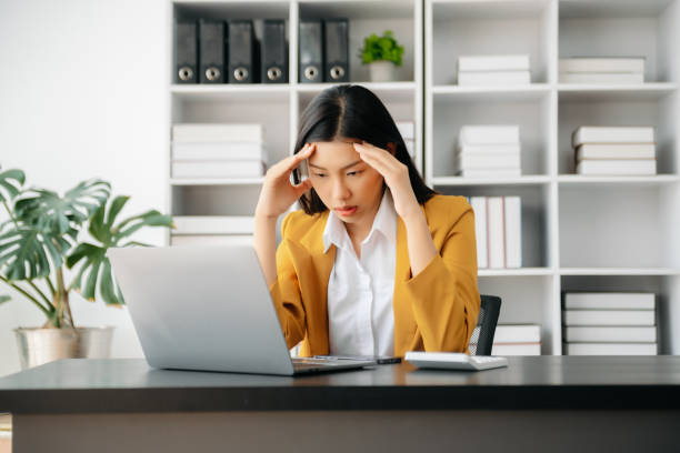 азиатская женщина, испытывающая мигрень, напряжение головы. перегруженная работой бизнесвумен-финансистка во время работы на ноутбуке и п� - 5956 стоковые фото и изображения