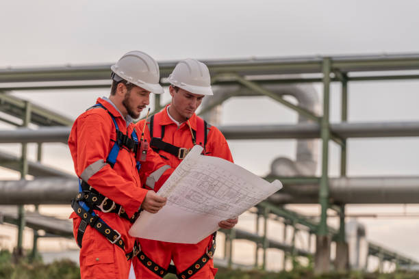 istock Engineer survey team wear uniform and helmet stand workplace checking blueprint project , radio communication and engineer box inspection work construction site with oil refinery background. 1807043811