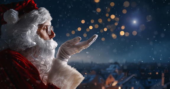 Merry Christmas and happy holidays. Santa Claus blowing snow and looking at the night city.