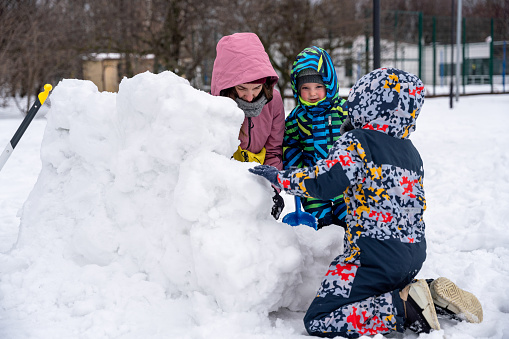 Mother with two sons building a snow fort at public park. Family outdoors leisure activity
