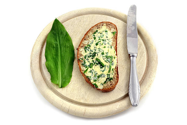 herb butter wild garlic (Allium ursinum) on slice of bread at wooden cutting board and kitchen knife. white isolated background