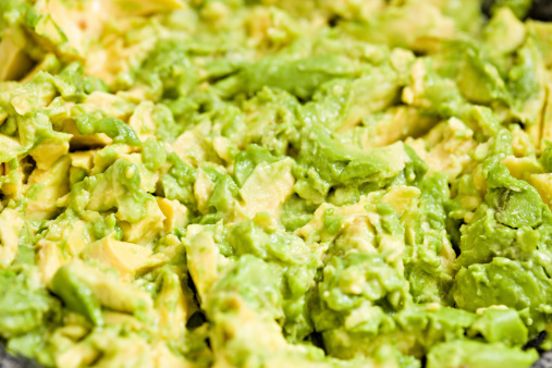 A high angle extreme close up shot of smashed avocado in a bowl.