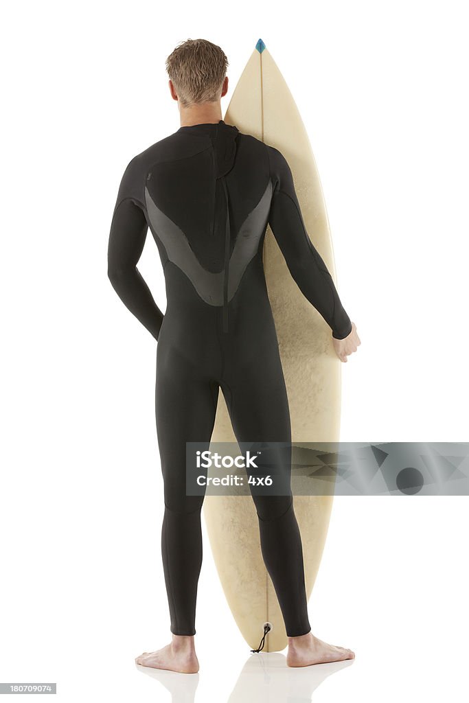 Vista posterior de un hombre de pie con tabla de surf - Foto de stock de 18-19 años libre de derechos
