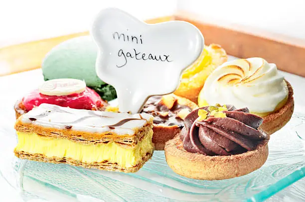 "Plate of mini-cakes; a green meringue, a lemon meringue tart, chocolate mousse, apricot tart, custard slice, and chocolate custardMore like this"