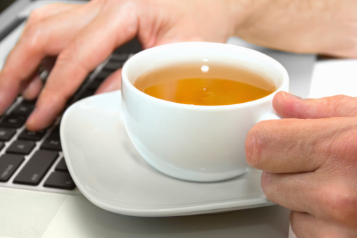 man's hand holding a cup of green tea while working at the computer