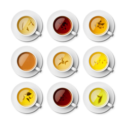 An overhead view of different teas isolated on a white background with a clipping path. From top left across first, Jasmine, Assam Black, Green Chai, White English Breakfast, Snow Dragon, Chamomile and Lavender, Japanese Bancha, Rooibos and Green Tea. Individually served in a white cup and saucer.