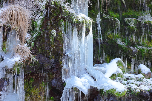 Cold winter temperatures caused the spray from a waterfall in the Adirondacks to freeze and form beautiful intricate ice formations along the edge of the waterfall. The sun is beginning to set in the background, and the presence of tannins in the water can be seen by the tan and brown tint to the water.