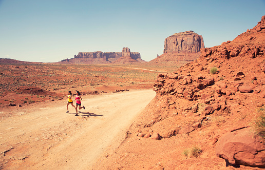 Two females trail run through the rock monuments of Monument Valley.