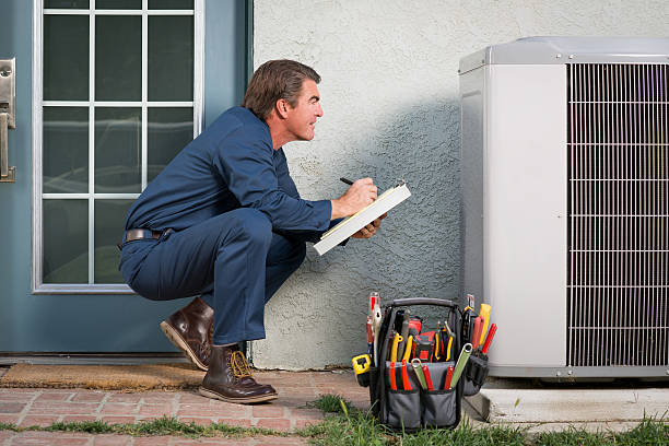 Air Conditioner Repairman Air conditioner repairman in uniform with a clipboard and tool bucket inspecting the AC unit.Take a look at my LIGHTBOXS with other related images. door repairman men manual worker stock pictures, royalty-free photos & images