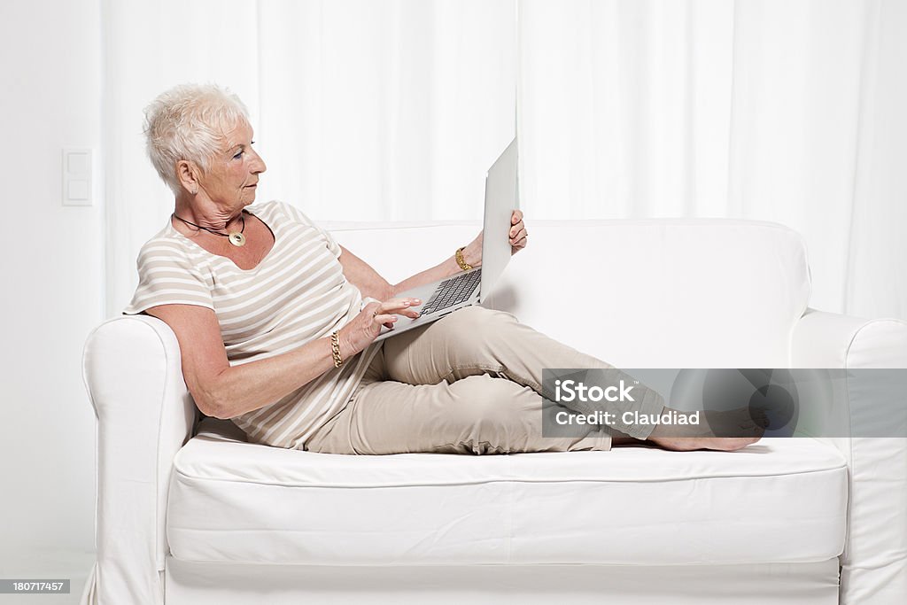 Sênior mulher em um sofá com laptop - Foto de stock de Foto de estúdio royalty-free