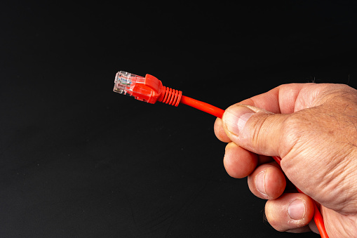 Man's hand holding internet cable on black background close up