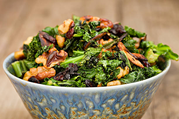 Cooked Kale "An extreme close up frontal shot of a blue bowl full of sautAed kale with walnuts, garlic slivers and dry cranberries." cruciferous vegetables stock pictures, royalty-free photos & images